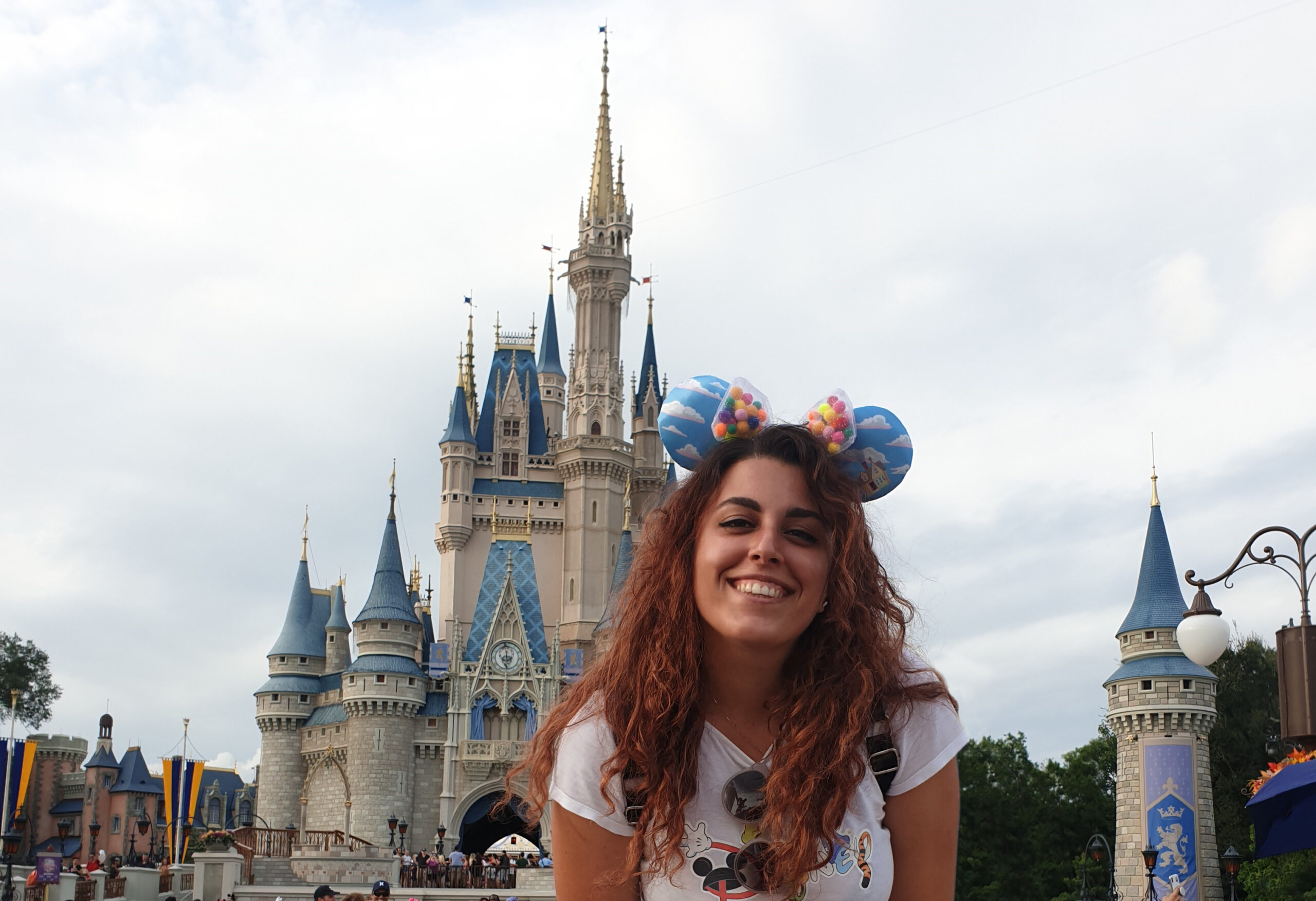 Carlotta sorridente davanti al castello di DisneyWorld a Orlando, in Florida. Indossa una t-shirt con la scritta Disney ed ha le orecchie di Topolino in testa.