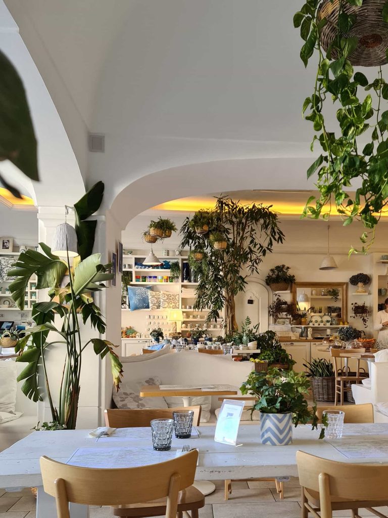 Foto scattata all'interno del ristorante Casa e Bottega a Positano. Si vedono dei tavoli apparecchiati e tante piante verdi.