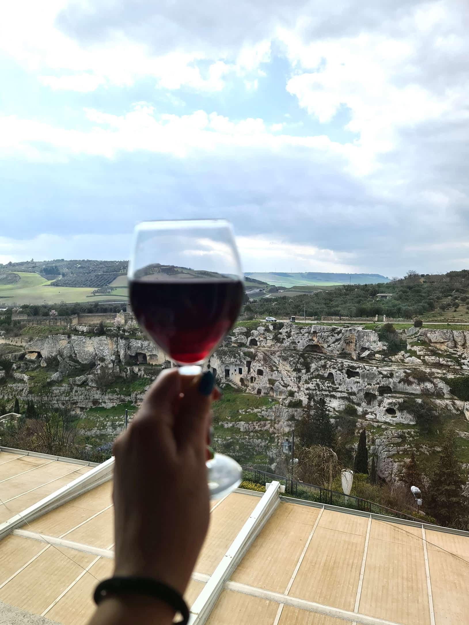 In foto si vede un bicchiere di vino rosso e il bellissimo panorama del complesso delle sette camere