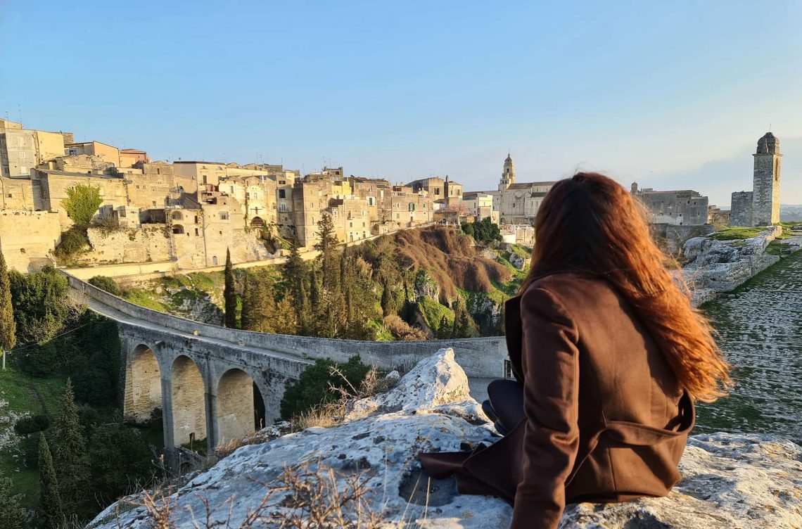 Carlotta seduta su una roccia, mentre guarda il panorama sulla città di Gravina in Puglia e sul suo ponte acquedotto.