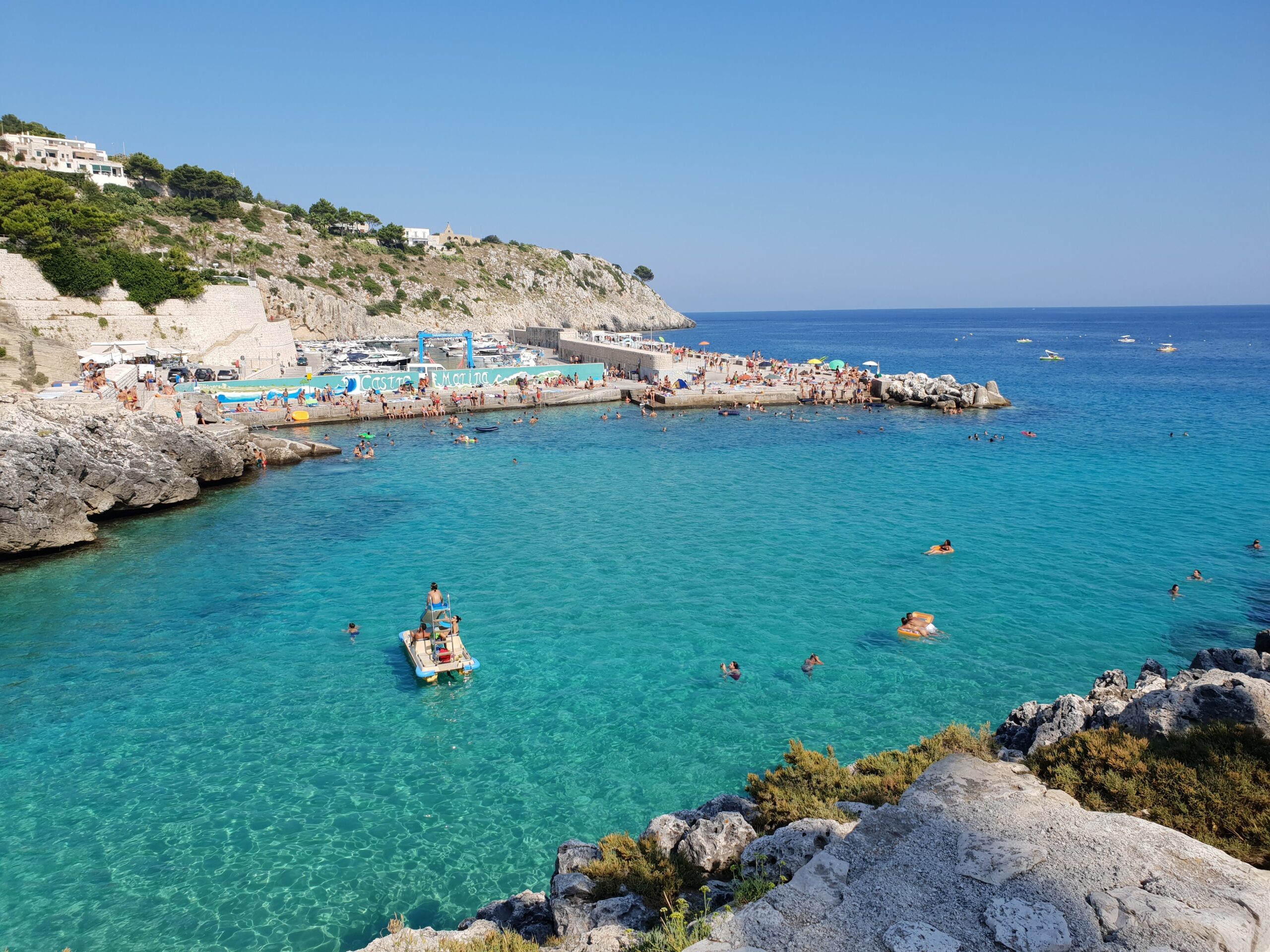 In foto si vede Castro Marina, con un mare azzurro che sembra quasi una piscina e dei pedalò che sembrano volare sull'acqua