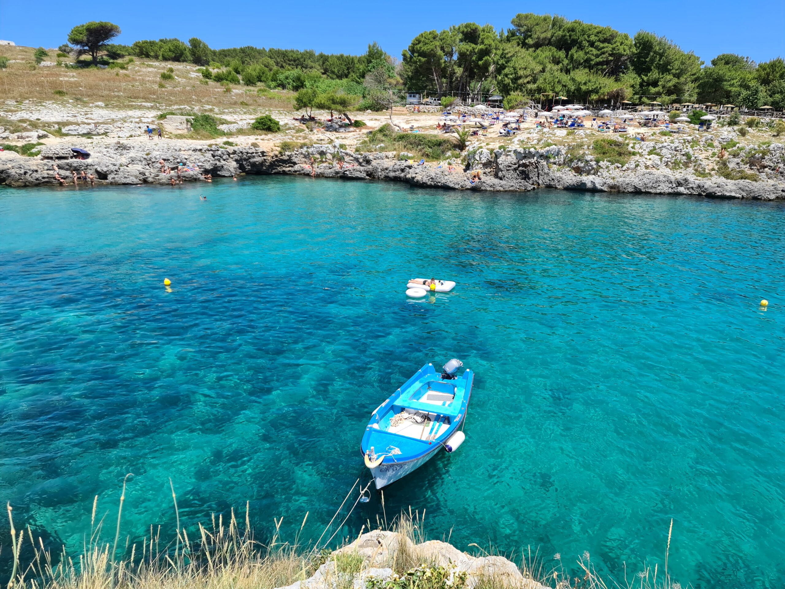 Una barchetta blu che galleggia su un mare azzurro e trasparente a porto Badisco