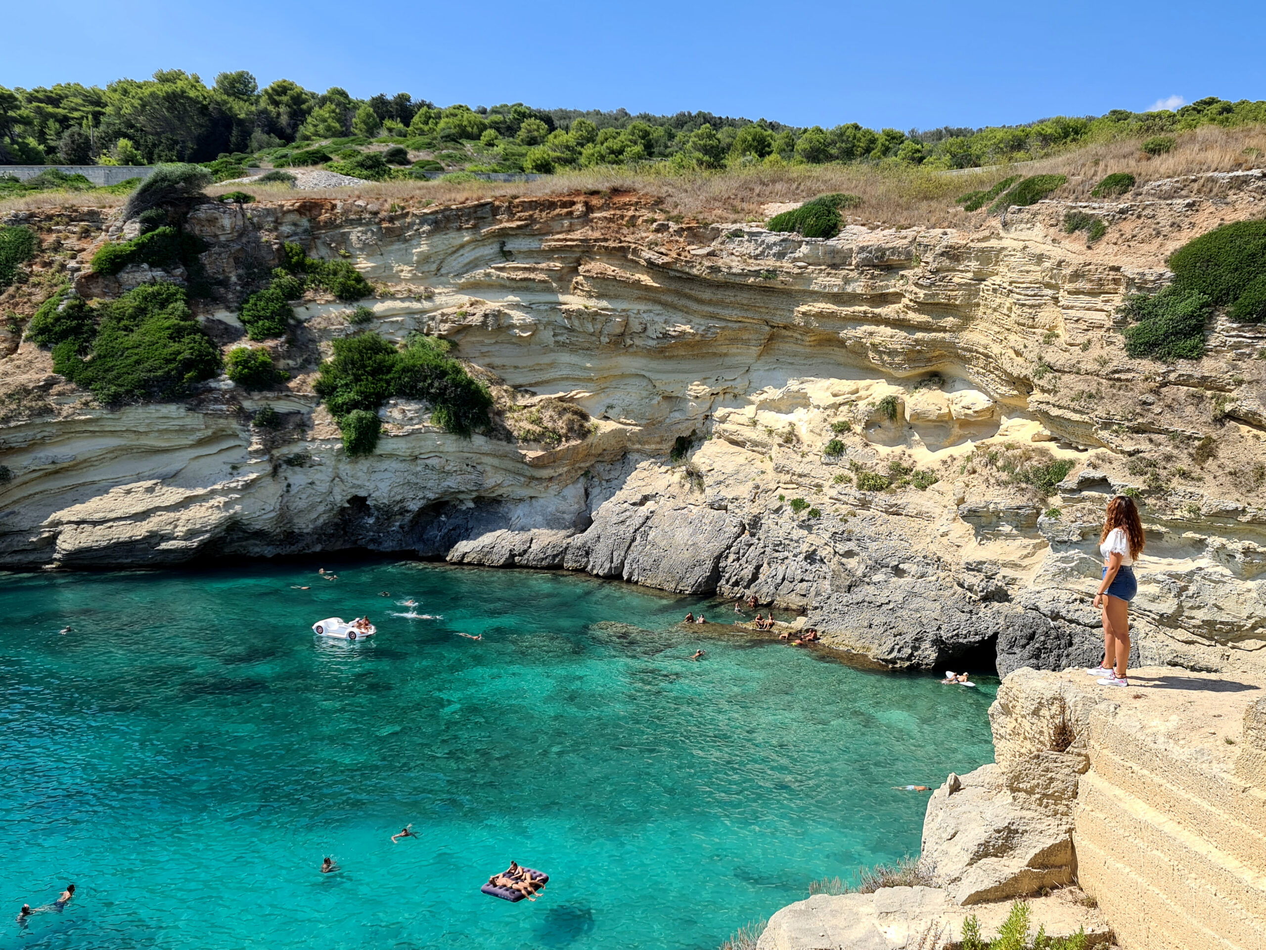 Carlotta in piedi mentre guarda la baia di Porto Miggiano, in Salento sulla Costa Adriatica, le cui pareti di roccia sembrano un gelato variegato alla nocciola.