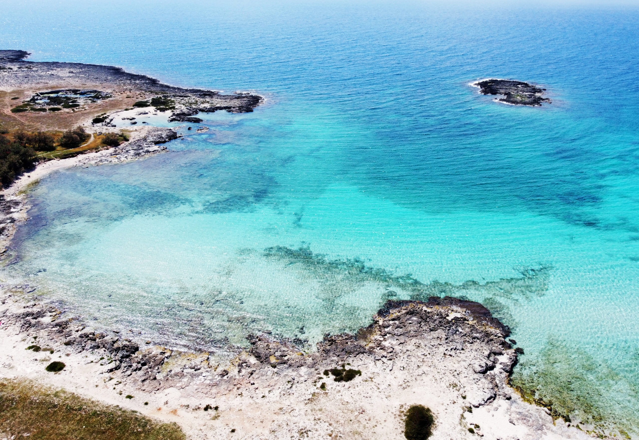 Ripresa dall'alto della spiaggia del Frascone. Mare limpido dalla tonalità azzurra, con un isolotto a forma di teschio in mezzo al mare.