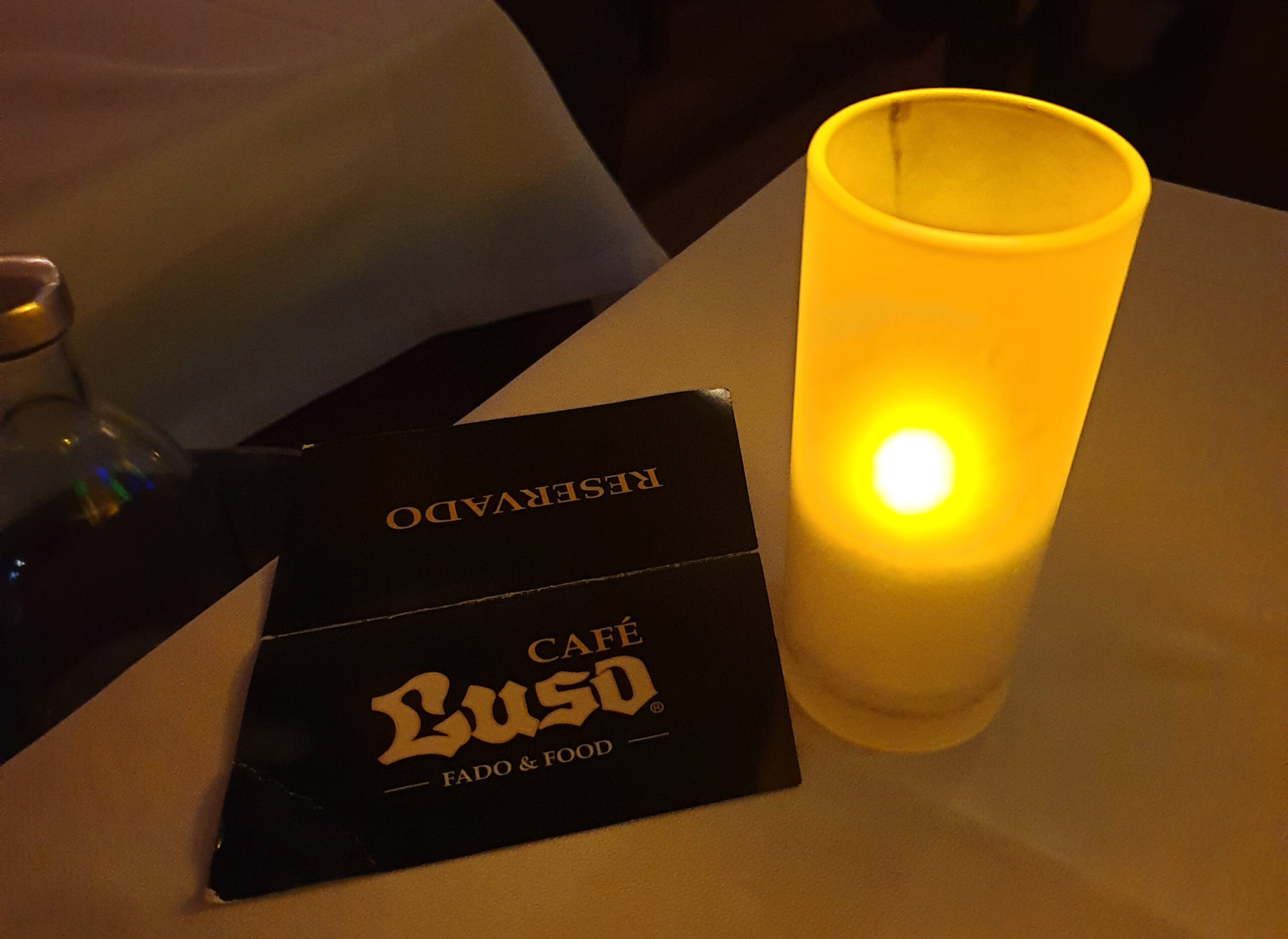 In foto si vede una candela accesa su una tovaglia bianca ed un cartoncino con scritto cafe Luso, il nome del ristorante