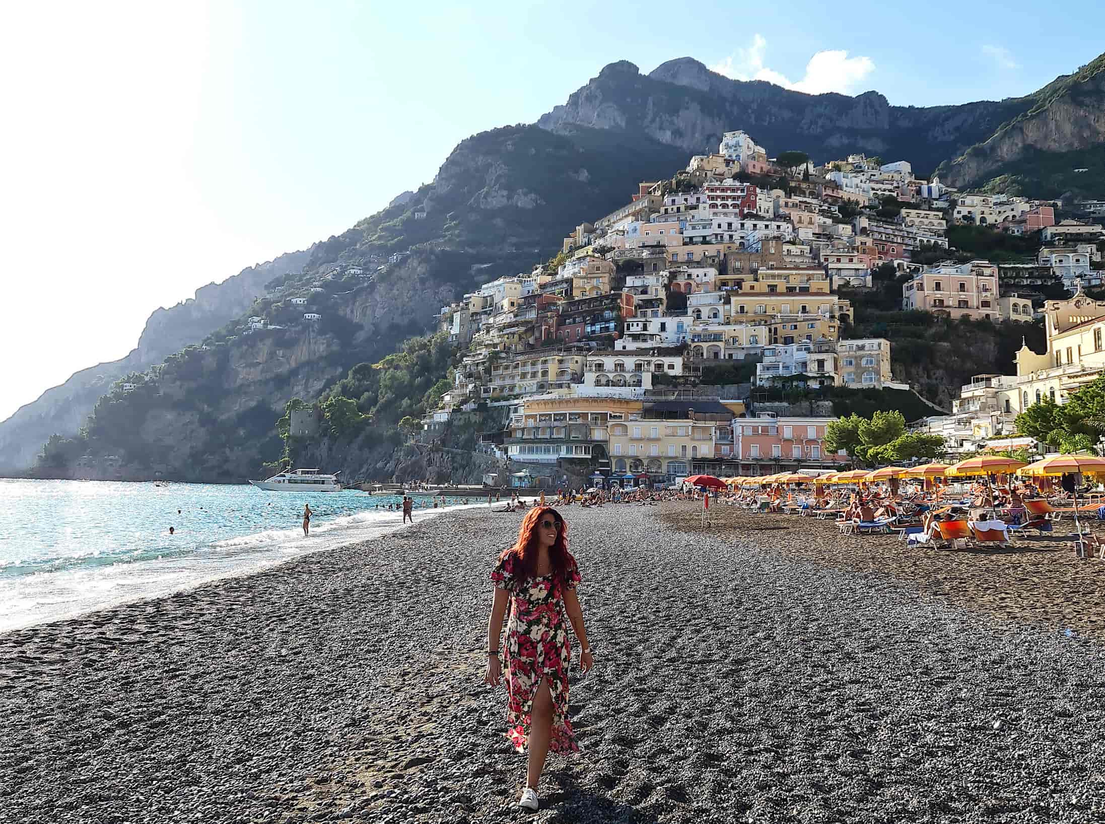 Carlotta mentre passeggia sulla spiaggia ciottolosa di Positano. Alle sue spalle la piramide di casette colorate che caratterizza la cittadina della costiera amalfitana
