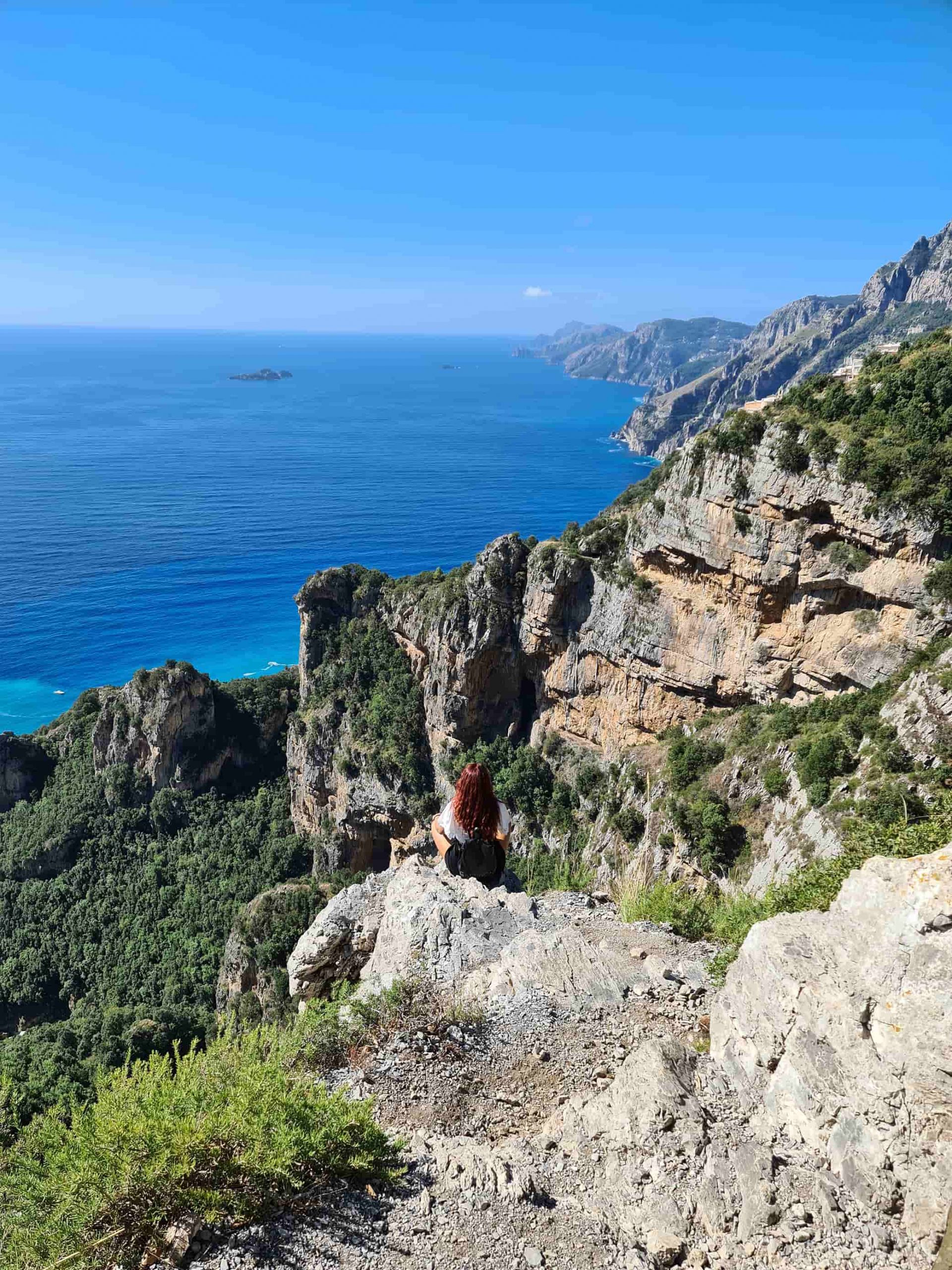 Carlotta di spalle seduta su una roccia a strapiombo durante il Sentiero degli Dei, mentre guarda il panorama sulla Costiera Amalfitana