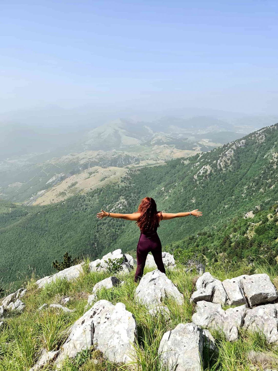Carlotta in piedi a braccia aperte mentre osserva il panorama sulle montagne dalla cresta di Serra del Prete