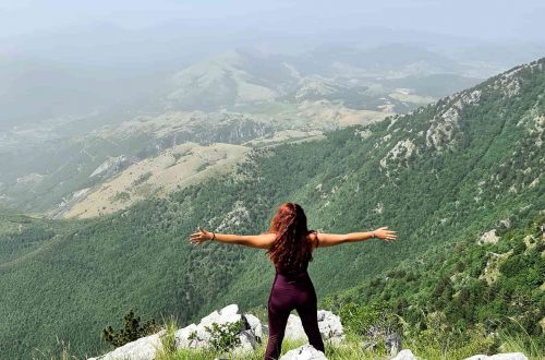 Carlotta in piedi a braccia aperte mentre osserva il panorama sulle montagne dalla cresta di Serra del Prete