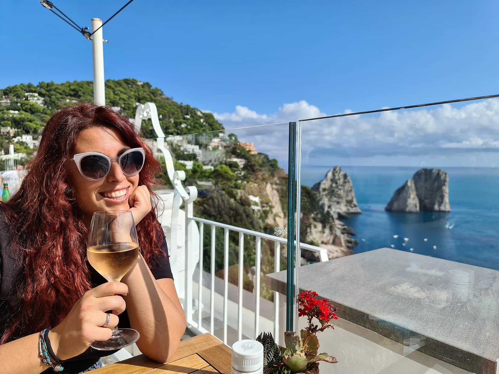 Carlotta con un calice di vino bianco in manco su una terrazza panoramica con vista sui faraglioni di Capri