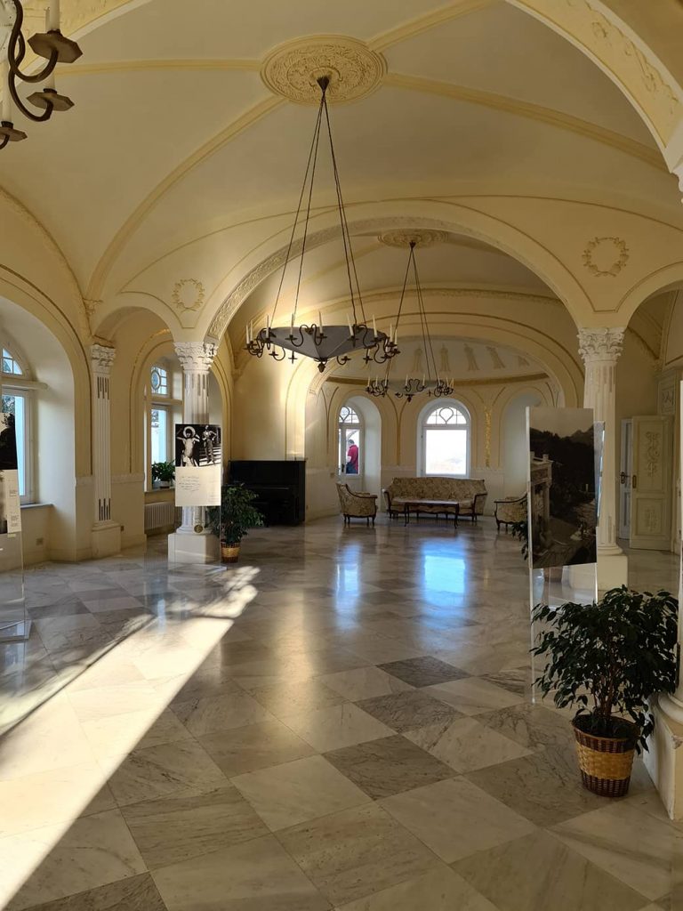 Una delle sale di Villa Lysis, tinteggiata di giallo paglierino, con un pianoforte addossato ad un muro e delle poltroncine. Il pavimento è come una scacchiera