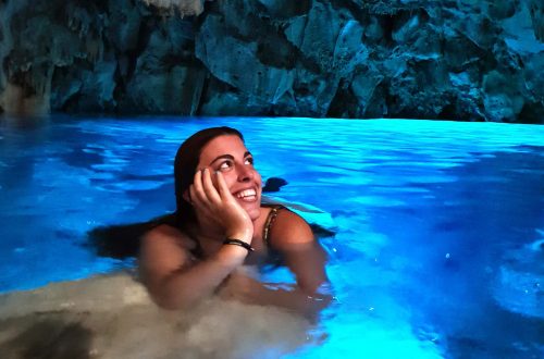 Carlotta appoggiata ad uno scoglio nella grotta del lago, mentre guarda le pareti della grotta colorate di azzurro e sorride