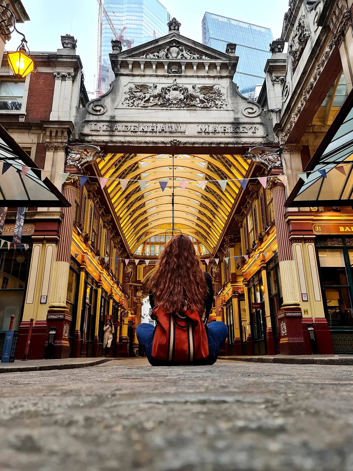 In foto si vede Carlotta di spalle, seduta per terra mentre guarda verso il Leadenhall Market, il primo dei luoghi di Harry Potter a Londra, caratterizzato da uno stile vittoriano, con una cupola vetrata e tante luci calde.