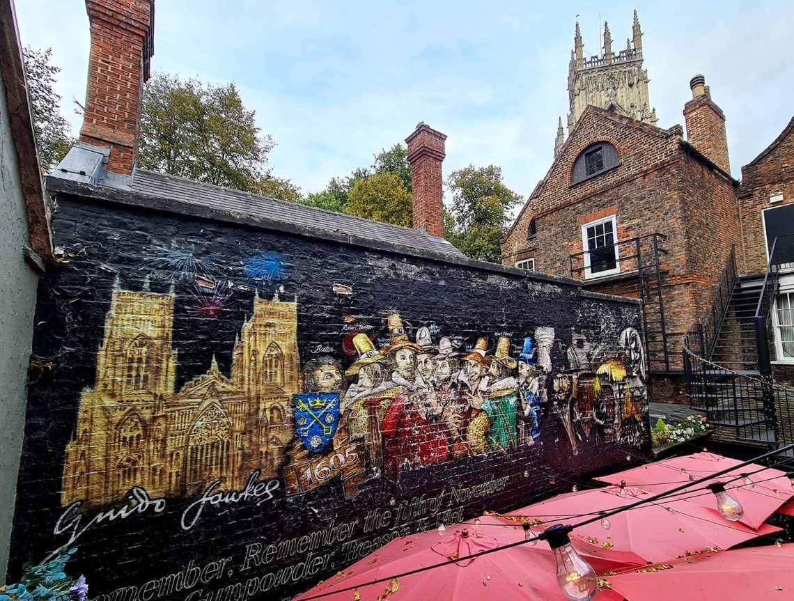 In foto si vede un grande murales che rappresenta la città di York e Guy Fawkes, durante la congiura delle polveri con la maschera di V per vendetta