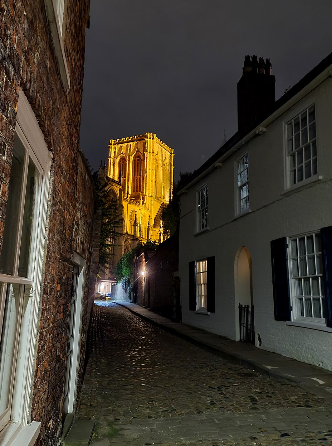 In foto si vede una delle torri della cattedrale gotica di York, immersa in un cielo scuro e nuvoloso, di sera. S'intravede anche una strada deserta, molto spettrale