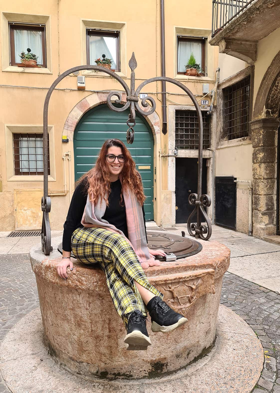 Carlotta sorridente, seduta su un pozzo in pietra, in un vicolo di questa Verona Insolita