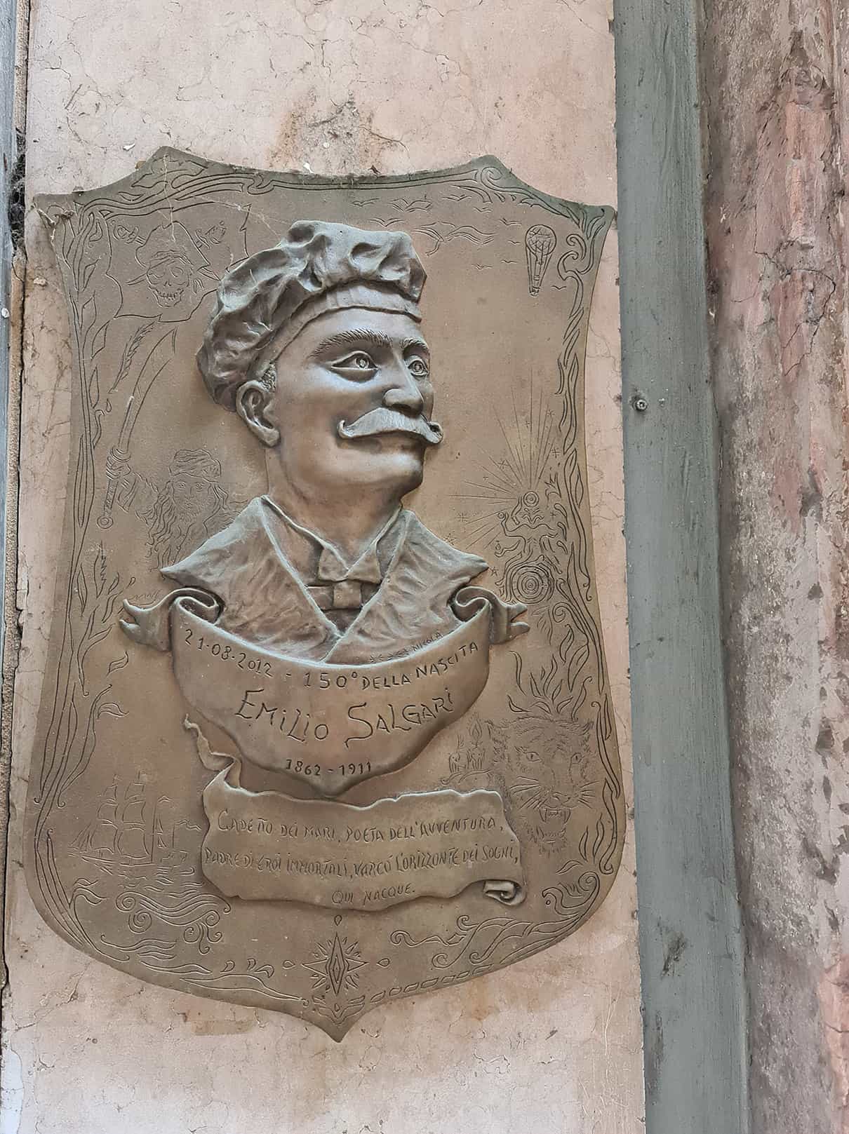 in foto si vede un bassorilievo in bronzo che raffigura la faccia baffuta di Emilio Salgari, che nacque su corso Borsari al civico 7
