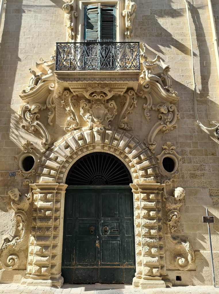 Una foto della facciata particolarmente elaborata di un palazzo con al centro un portone verde circondato da Angeli intagliati nel muro.