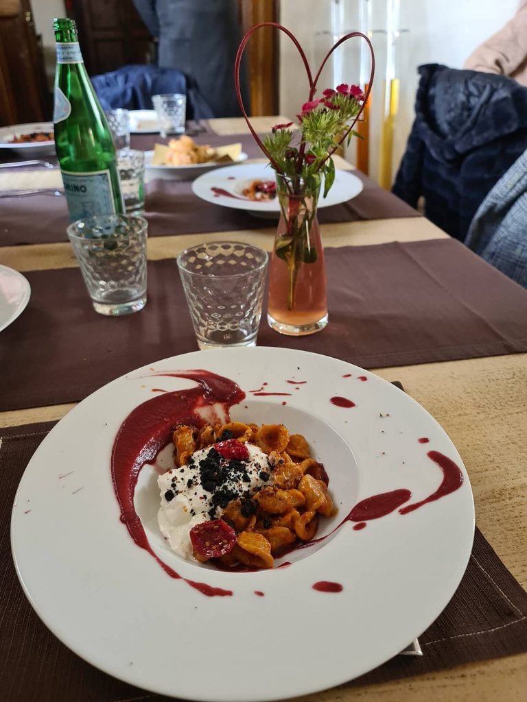 la foto di un piatto di orecchiette con crema di barbabietola rossa, stracciatella e crumble di olive nere.